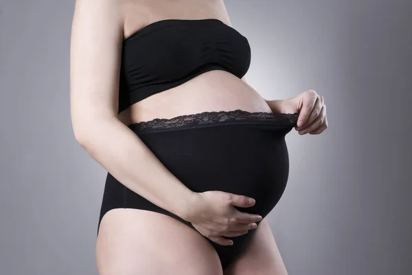 Mujer embarazada en bragas de apoyo negro sobre fondo gris — Foto de Stock