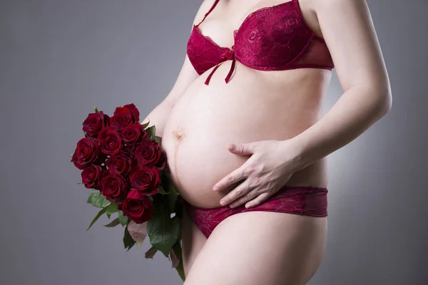 Jeune beauté et sexy femme enceinte caucasienne avec bouquet de roses rouges sur fond gris — Photo