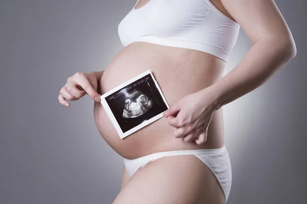 Pregnant woman in white underwear with baby ultrasound scan on gray background — Stock Photo, Image