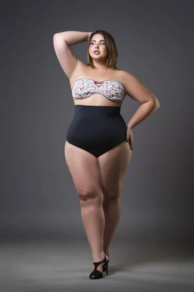 Plus-Size-Modell im sexy Badeanzug, junge dicke Frau auf grauem Hintergrund, übergewichtiger weiblicher Körper — Stockfoto