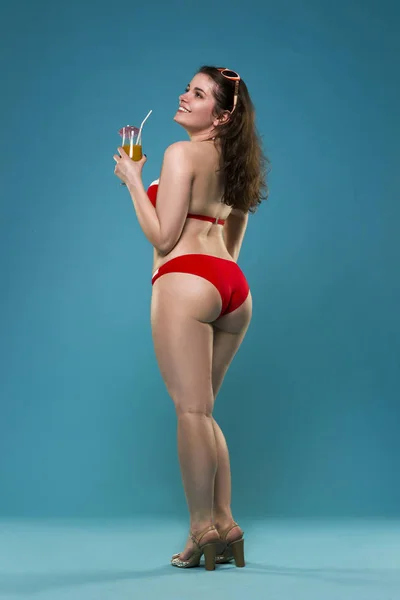 Красивая молодая женщина в красном бикини с коктейлем на синем фоне — стоковое фото