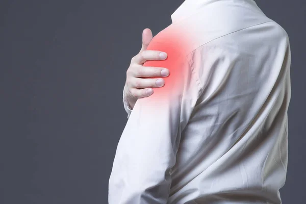 Человек с болью в плече на сером фоне — стоковое фото