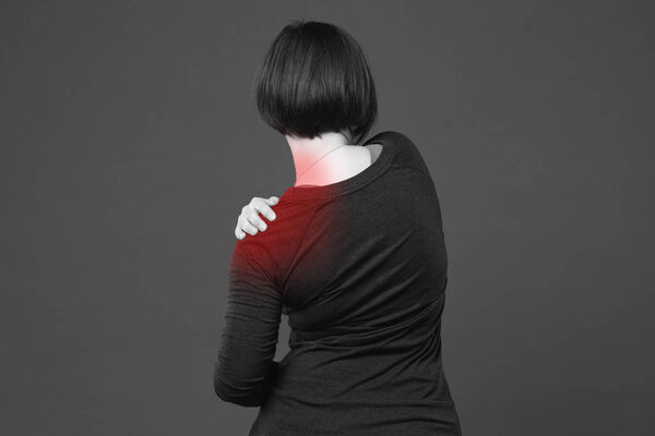 Woman with pain in shoulder on gray background