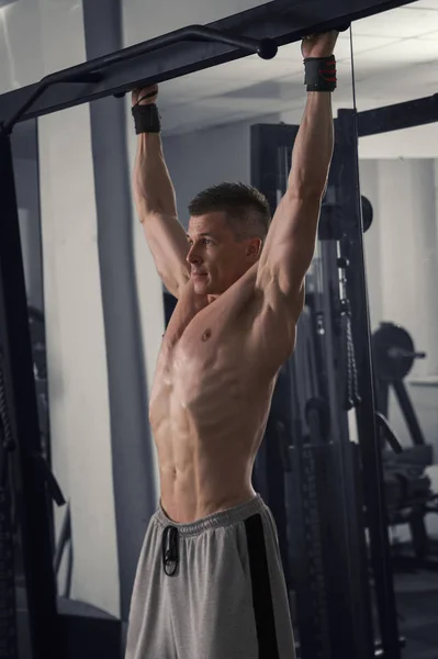 Culturista se detiene en el gimnasio, hombre musculoso realizar ejercicios en la barra horizontal —  Fotos de Stock