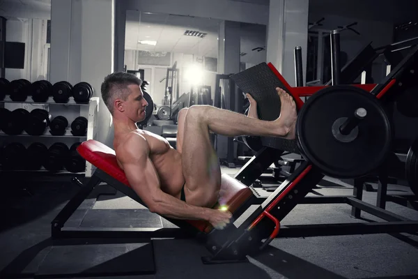 Muscular legs, handsome bodybuilder workout on trainer in the gym — Stock Photo, Image