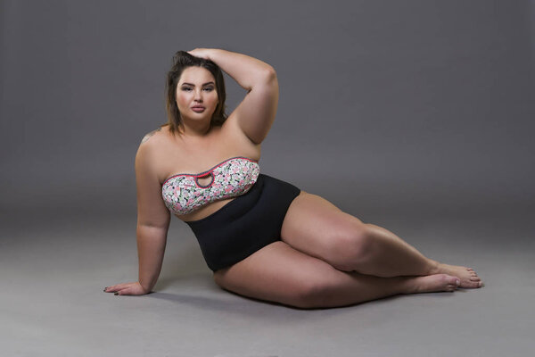 Plus size fashion model in sexy swimsuit, young fat woman on gray background, overweight female body