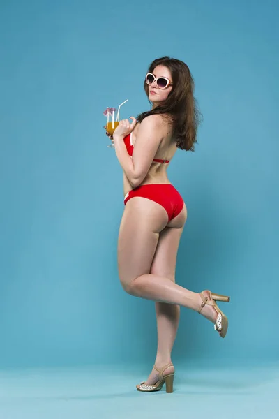Красивая молодая женщина в красном бикини с коктейлем на синем фоне — стоковое фото