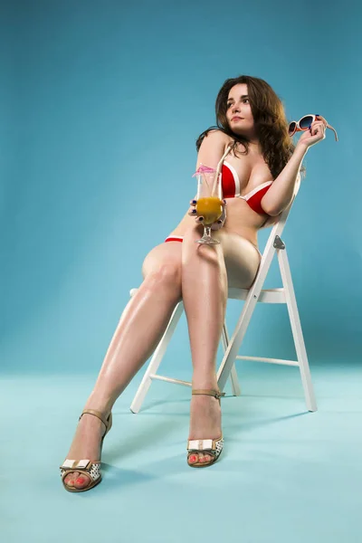 Krásná mladá žena v červené bikiny s koktejlem na modrém pozadí — Stock fotografie