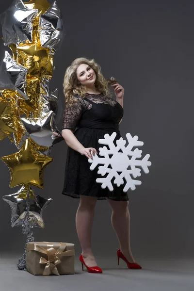 Плюс женщина в черном платье с подарочной коробкой, снежинкой и воздушными шариками на заднем плане — стоковое фото