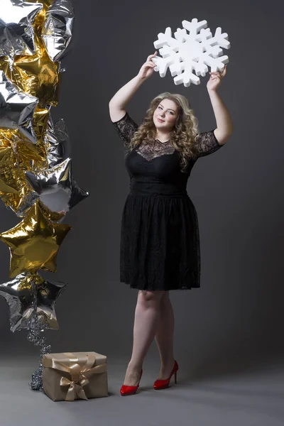 Plus size Frau in schwarz dres mit Geschenkbox, Schneeflocke und Luftballons auf grauem Hintergrund — Stockfoto