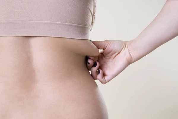 Mulher segurando dobra de pele, celulite no corpo feminino, fundo bege — Fotografia de Stock