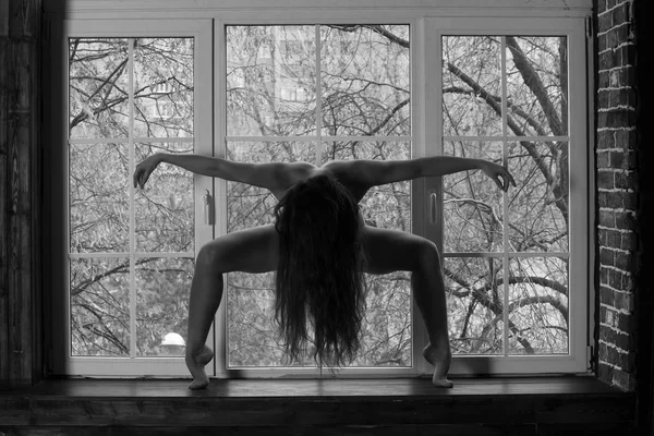 Naked yoga, flexible nude sexy body of young woman on window