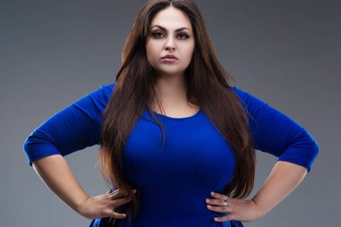 Artı mavi elbiseli bir model, gri arka planda uzun saçlı şişman bir kadın, vücut pozitifliği