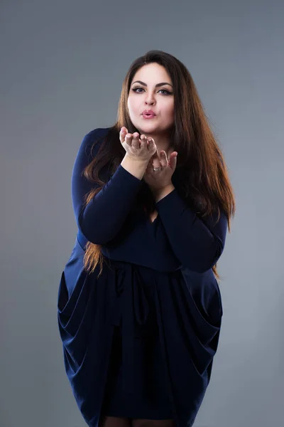 Plus size model in blue dress sends air kiss, fat woman with long hair on gray background, body positive concept — Stock Photo, Image