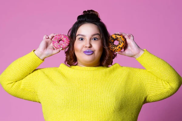 Alegre modelo de talla grande con rosquillas, mujer gorda feliz sobre fondo rosa — Foto de Stock