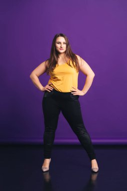 Artı günlük kıyafetlerle manken boy, mor arka planda şişman bir kadın.