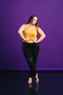 Artı günlük kıyafetlerle manken boy, mor arka planda şişman bir kadın.