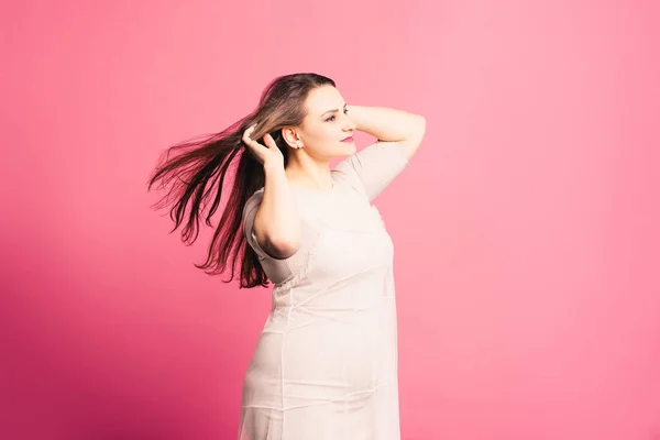 Плюс модель размера с длинными волосами на ветру, толстая женщина на розовом фоне — стоковое фото