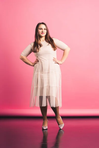 Plus velikost módní model v béžových šatech, tlustá žena na růžovém pozadí — Stock fotografie