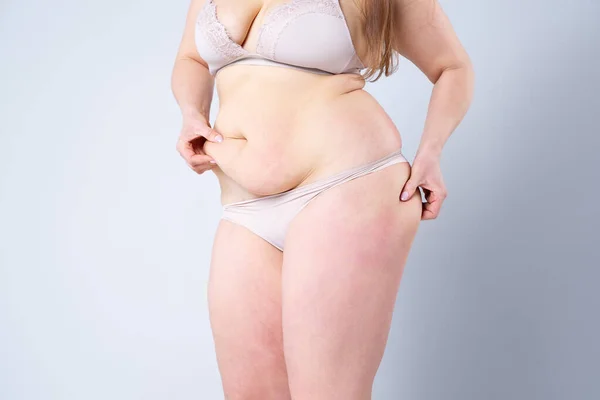 Tummy tuck, flabby skin on a fat belly, plastic surgery concept on gray background