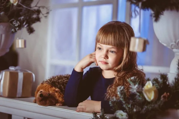 Little girl dreams of a holiday on the Christmas window decoration — Stock Photo, Image