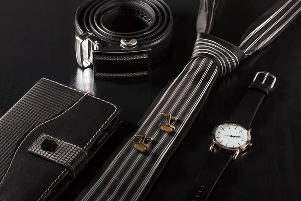 Notebook, tie, cufflinks, leather belt, watch on a black backgro