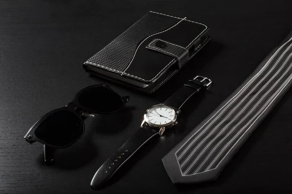 Reloj, cuaderno, gafas de sol, corbata sobre fondo negro — Foto de Stock
