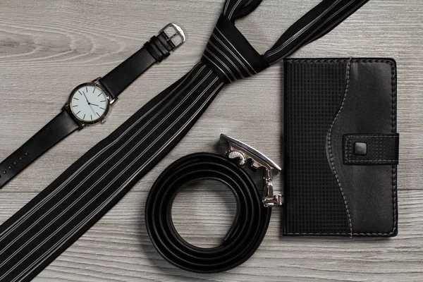 Leather belt, watch, silk tie, notebook on a gray wooden backgro