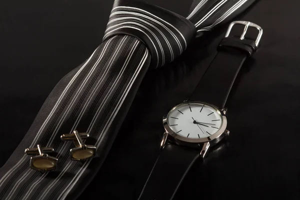 Шелковый галстук, запонки, часы на черном фоне — стоковое фото