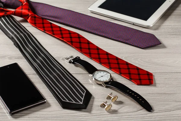 Corbatas de seda de color, reloj, gemelos y dispositivos móviles sobre un fondo de madera gris — Foto de Stock
