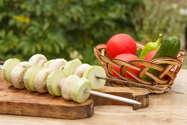 Zucchini and mushrooms on metal skewers on wooden chopping board — Stock Photo, Image