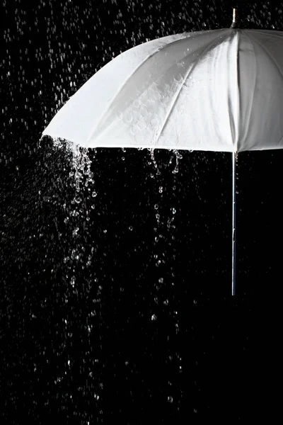 Guarda-chuva branco sob gotas de chuva com fundo preto — Fotografia de Stock