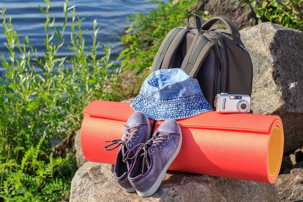 Zaino da trekking, sneakers, cappello, macchina fotografica e tappetino da campeggio su roccia — Foto Stock