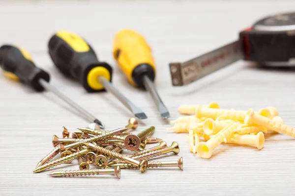 Screwdrivers, tape measure and screws on white wooden background