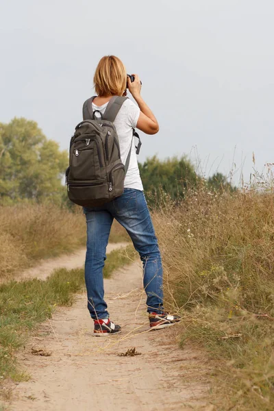 Jovem caminhando em uma estrada rural com câmera digital — Fotografia de Stock