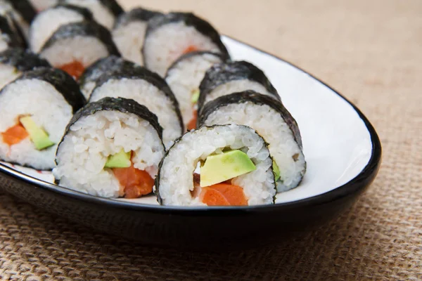 Rollos de sushi en algas nori con aguacate y pescado rojo en cerámica — Foto de Stock