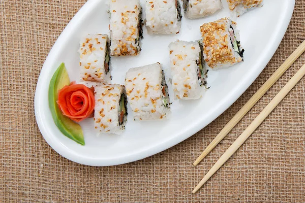 Rollos de sushi uramaki con aguacate y pescado rojo en plato de cerámica a — Foto de Stock