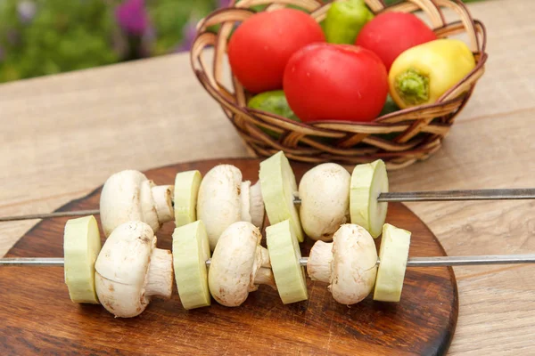 Zucchini and mushrooms on metal skewers on wooden chopping board — Stock Photo, Image