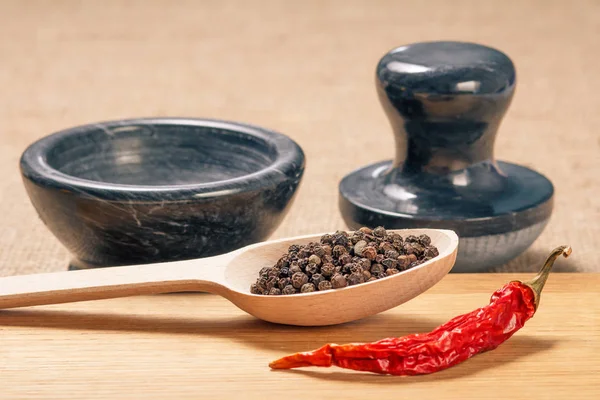 Wooden spoon with black peppercorn, dried red pepper on cutting