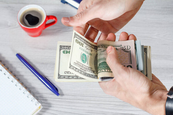 Человек держит и считает долларовые купюры
