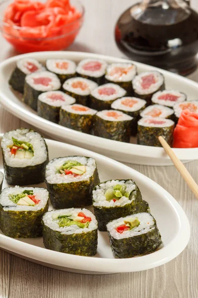 Diferentes rollos de sushi en plato de cerámica, palillos, botella de vidrio — Foto de Stock