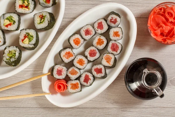 Diversi rotoli di sushi su piatto di ceramica, bacchette, bottiglia di vetro — Foto Stock