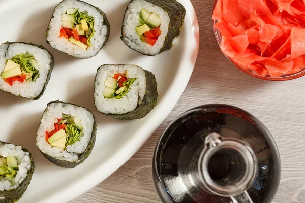 Rotoli di sushi con riso su piatto di ceramica, bottiglia di vetro con soia sa — Foto Stock