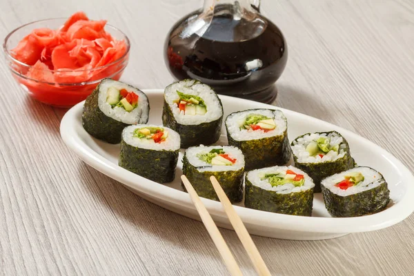 Rolos de sushi com arroz em prato cerâmico, pauzinhos, garrafa de vidro — Fotografia de Stock