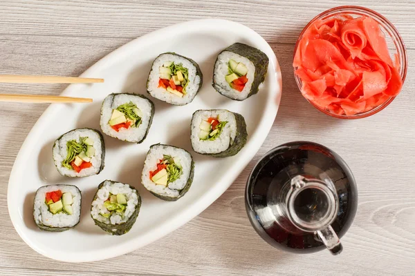 Rotoli di sushi con riso su piatto di ceramica, bacchette, bottiglia di vetro — Foto Stock