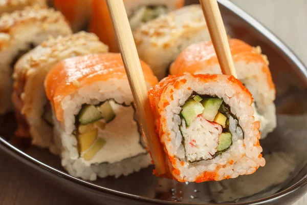 Due bacchette che tengono Uramaki California e sushi diverso r — Foto Stock