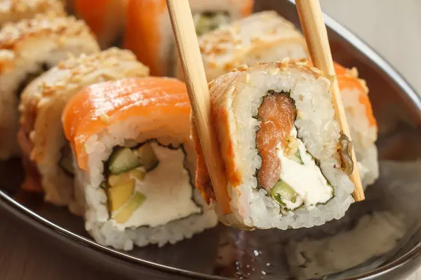 Due bacchette che tengono Uramaki con Conger e sushi diverso — Foto Stock