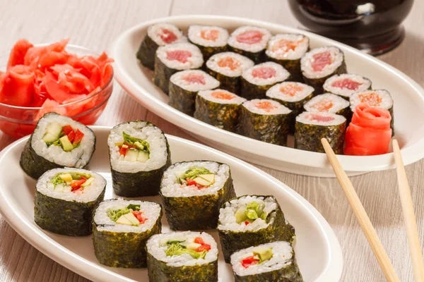 Diversi rotoli di sushi su piatto di ceramica, bacchette, bottiglia di vetro — Foto Stock