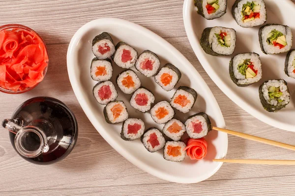 Diferentes rollos de sushi en plato de cerámica, palillos, botella de vidrio — Foto de Stock