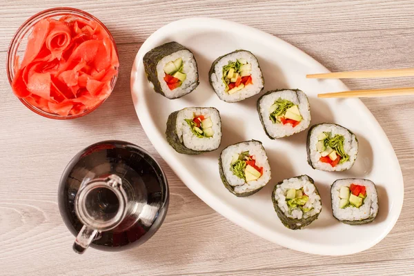 Rotoli di sushi con riso su piatto di ceramica, bacchette, bottiglia di vetro — Foto Stock